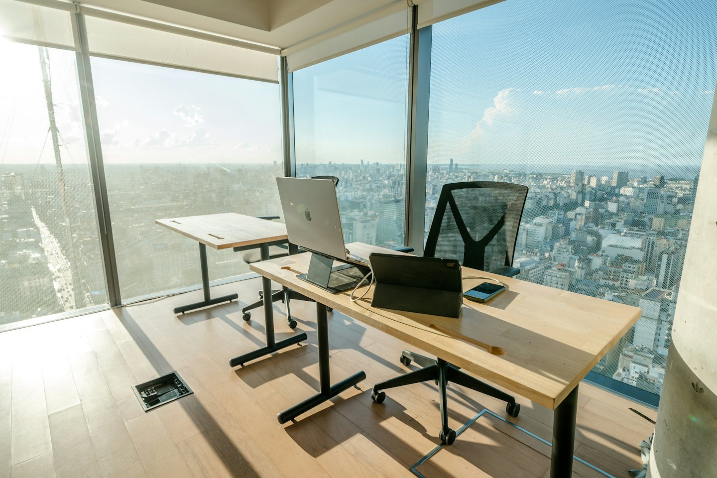 Scrivanie d'ufficio moderne con laptop affacciate su uno skyline cittadino.