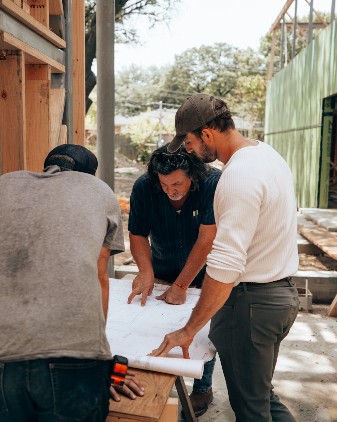 Tre professionisti dell'edilizia esaminano delle planimetrie in un cantiere all'aperto.