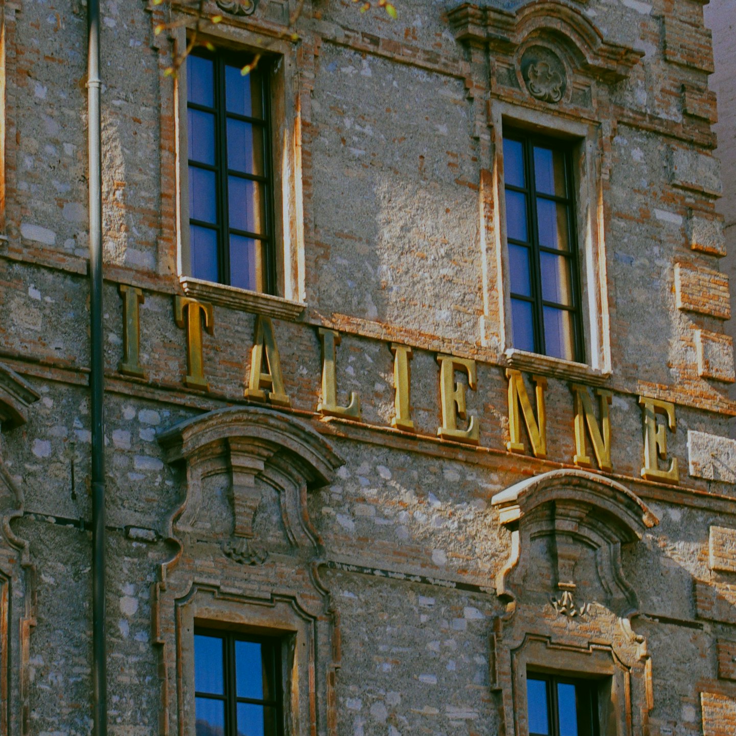 Facciata ornata di un edificio in pietra e mattoni con lettere dorate che compongono la scritta Italienne.
